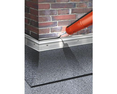 Abdichten einer Sockelleiste mit Dichtmasse vor einer Backsteinmauer