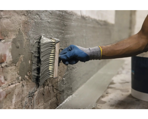 Handwerker trägt mit einer Bürste Dichtschlämme auf eine Ziegelwand auf.