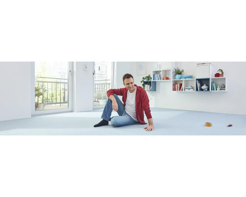 Ein Mann sitzt auf einem hellen Bodenbelag in einem hellen Raum mit einem Balkon.