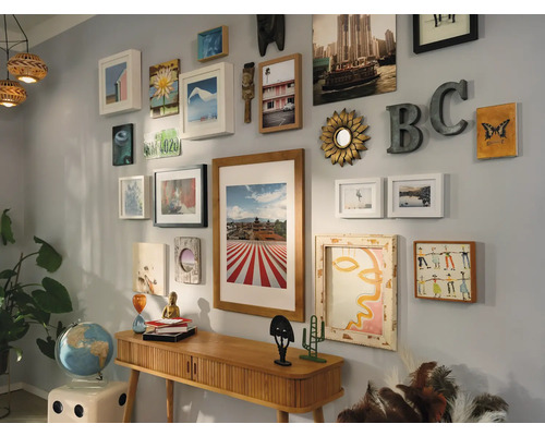 Wanddekoration mit Bildern, Spiegeln und dekorativen Objekten über einem Konsolentisch