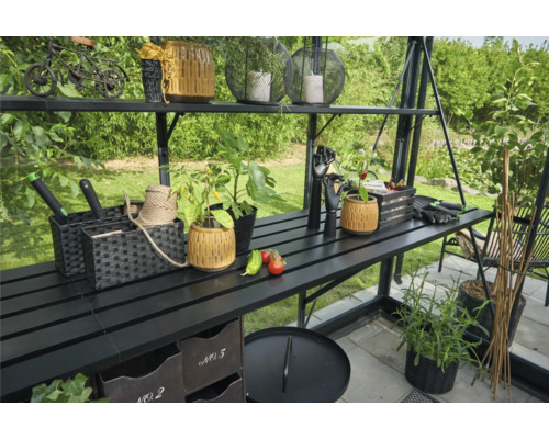 Gewächshaus mit Regalen und Gartenzubehör wie Töpfe, Pflanzen und Werkzeuge.