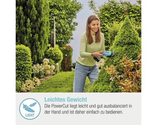 Eine Frau schneidet mit einer Akku-Grasschere einen Strauch im Garten.