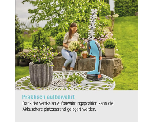 Akkubetriebene Grasschere und Strauchschere auf einem Gartentisch mit Frau im Hintergrund