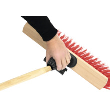 Eine Hand hält eine Kehrbürste mit Holzstiel und roten Borsten.