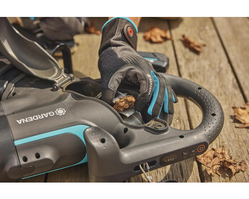 Gardena Akku-Laubsauger mit offener Klappe und Hand mit Gartenhandschuh, die Laub entfernt