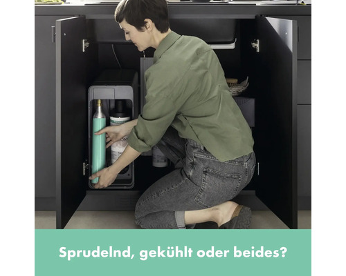 Frau verstaut Wassersprudler-Zubehör im Küchenschrank