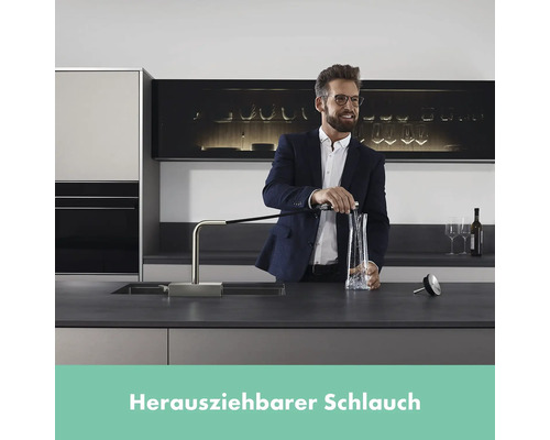 Mann füllt Wasser in eine Karaffe mit einer Spültischarmatur mit ausziehbarem Schlauch in einer modernen Küche.