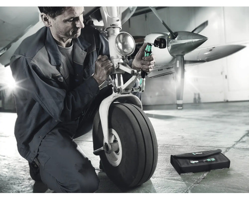 Ein Mechaniker repariert das Fahrwerk eines Flugzeugs mit Schraubendrehern und einer Werkzeugtasche.