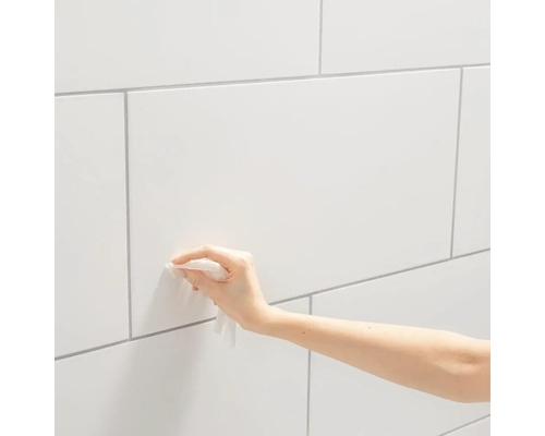 Eine Hand reinigt eine weiße geflieste Wand.