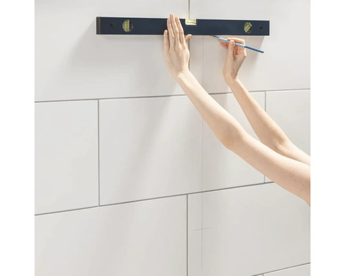 Eine Person verwendet eine Wasserwaage und einen Bleistift, um eine Linie an einer gefliesten Wand zu markieren.