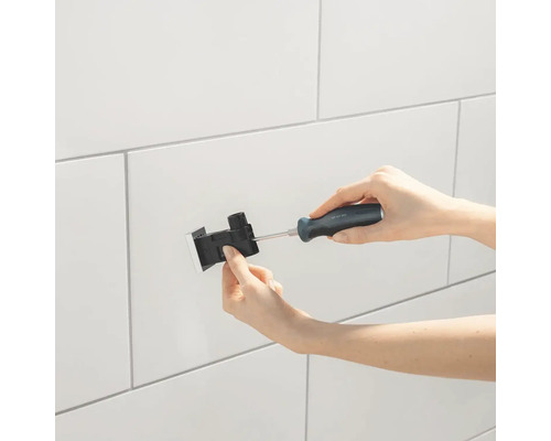 Installation eines Accessoires mit einem Schraubendreher an einer gefliesten Wand.