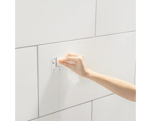 Eine Person befestigt eine Grohe Abdeckplatte auf einer gefliesten Wand.