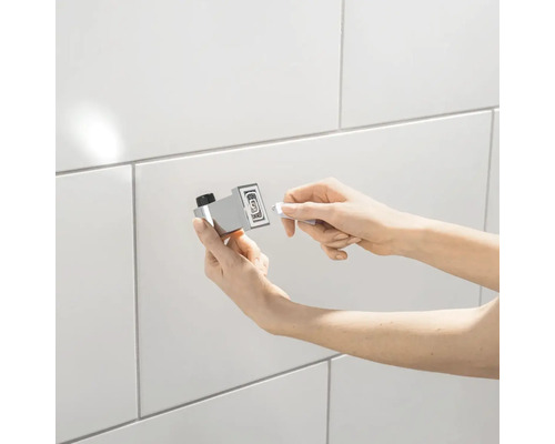 Person befestigt einen Handtuchhaken an einer gefliesten Wand.