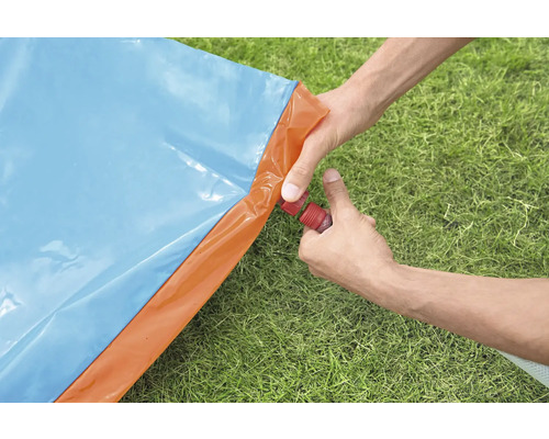Eine Person verbindet einen Wasserschlauch mit einer blauen und orangefarbenen Wasserrutsche im Garten.