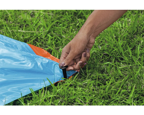 Person befestigt eine blaue Plane mit einem Hering im Gras