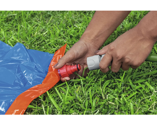Eine Person verbindet einen Gartenschlauch mit einer Wasserrutsche auf einer Rasenfläche.