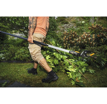 Eine Person schneidet mit einer Teleskop-Astschere Äste in einem Garten.