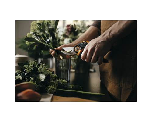 Eine Person schneidet mit einer Fiskars Gartenschere Zweige auf einem Tisch.