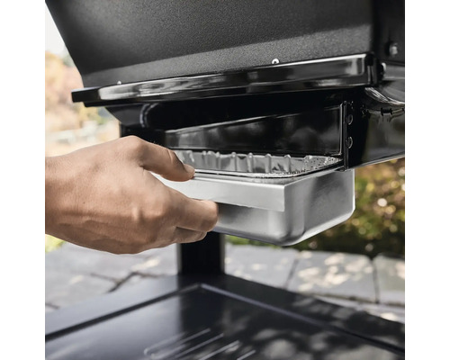 Hand zieht Fettschale eines Grills heraus.