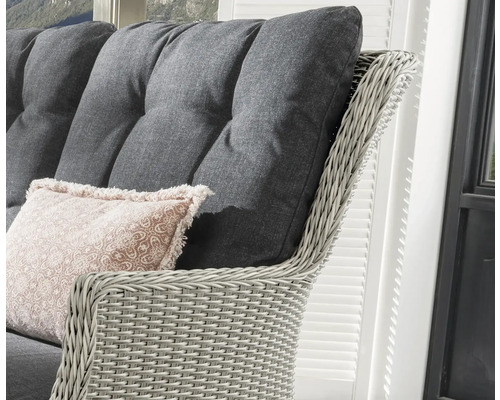 Nahaufnahme eines Rattansessels mit grauen Polstern und einem Zierkissen