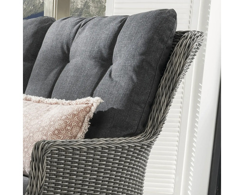 Detailansicht eines Rattansessels mit grauen Polsterkissen und Dekokissen
