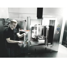 Mann bedient Industriewaschmaschine mit Warnsymbolen zu Vorsicht, Augenschutz und Rauchverbot