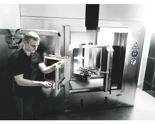 Mann bedient Industriewaschmaschine mit Warnsymbolen zu Vorsicht, Augenschutz und Rauchverbot