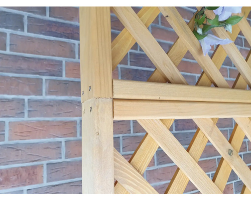 Detail einer Holzpergola mit Rankgitter vor einer Ziegelmauer.