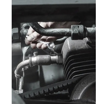 Hand schraubt Schraube an Motor mit Ratschenschlüssel fest