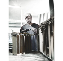 Handwerker arbeitet mit einem Akkubohrer an einem Holzobjekt in einer Werkstatt.