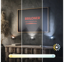 Drei Wandleuchten mit unterschiedlicher Lichtfarbe über einer Kommode und einem gerahmten Bild mit dem Briloner Logo