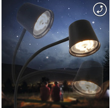 Dreiarmige Schreibtischlampe vor einem Hintergrund mit Personen und Zelten