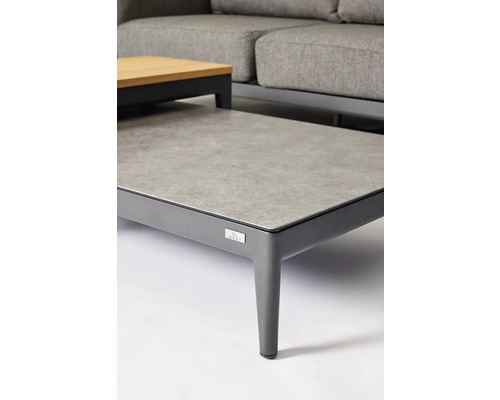 Detailansicht eines Gartentisches mit Steinplatte und Metallgestell, ergänzt durch ein graues Sofa im Hintergrund