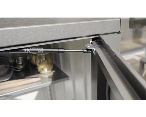 Detailansicht eines Gasdruckdämpfers an einem Gartenschrank.