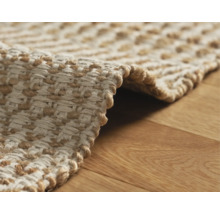 Detailansicht eines geflochtenen Teppichs aus Naturfasern auf einem Holzboden