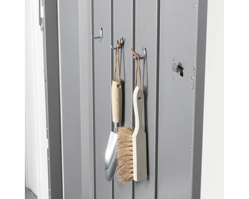 Gartengeräte wie eine Handschaufel und eine Bürste hängen an Haken in einem Geräteschuppen.
