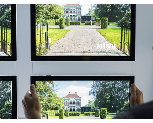 Mehrere beleuchtete Immobilienanzeigen mit Bildern von Häusern und Gärten hängen an einer Wand