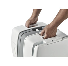 Zwei Hände heben eine tragbare Katzentoilette am Griff an.