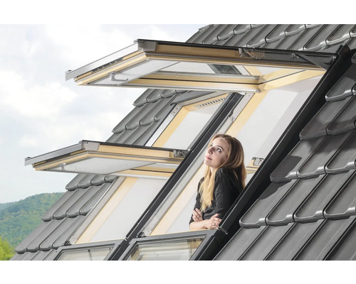 Frau schaut aus geöffnetem Dachfenster mit grauen Dachziegeln