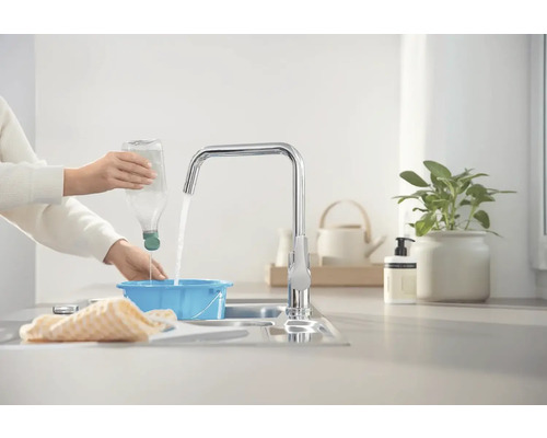 Eine Person füllt Wasser aus einer Flasche in eine blaue Schüssel unter einem Wasserhahn