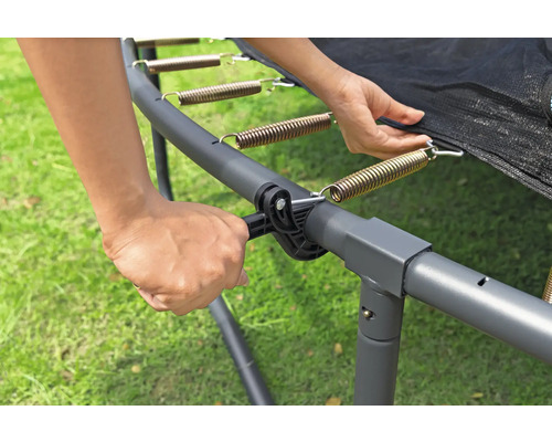 Person befestigt eine Feder am Trampolinrahmen mit einem Spannwerkzeug