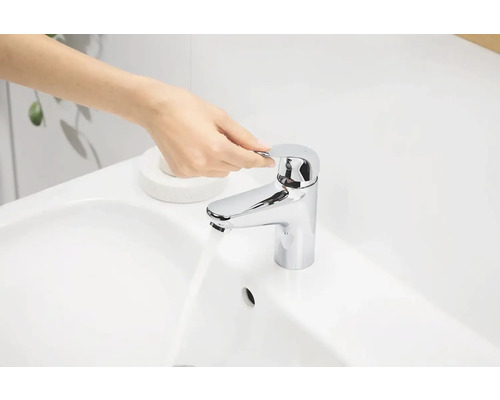 Eine Hand bedient einen glänzenden Wasserhahn an einem Waschbecken.