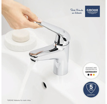 Eine Hand betätigt einen verchromten Waschtischmischer von Grohe, Wasser fließt. Garantie: 5 Jahre. Hergestellt in Deutschland. Grohe Logo.