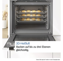 Geöffneter Backofen mit drei Ebenen Schokostückchen-Keksen auf Backpapier