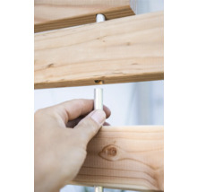 Detailansicht einer Holzkonstruktion mit silberfarbenen Metallstiften, die von einer Hand gehalten werden.