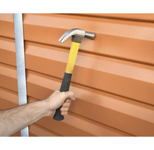 Eine Hand hält einen Hammer vor einer Wand.