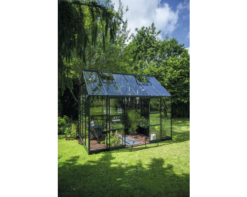 Gewächshaus mit Glaswänden und Pflanzen im Garten.