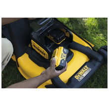 Eine Person setzt einen 18-Volt-Akku in einen gelben Rasenmäher von DeWalt ein.