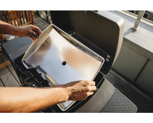 Person setzt eine Fettauffangschale in einen Grill ein.