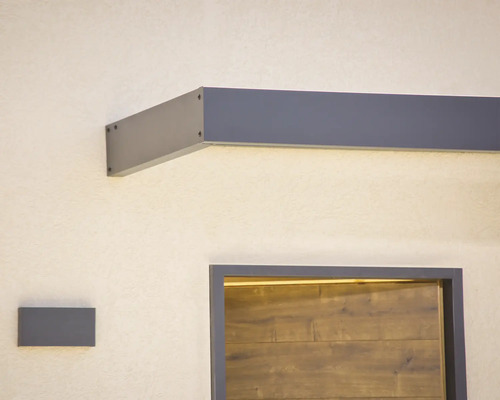 Modernes Vordach in Anthrazit mit integrierter LED Beleuchtung über einer Haustür in Holzoptik und passender Wandleuchte.